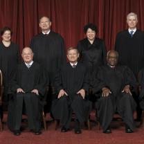Photo of men and women posing and facing the camera all wearing long black robes in front of a dark red curtain